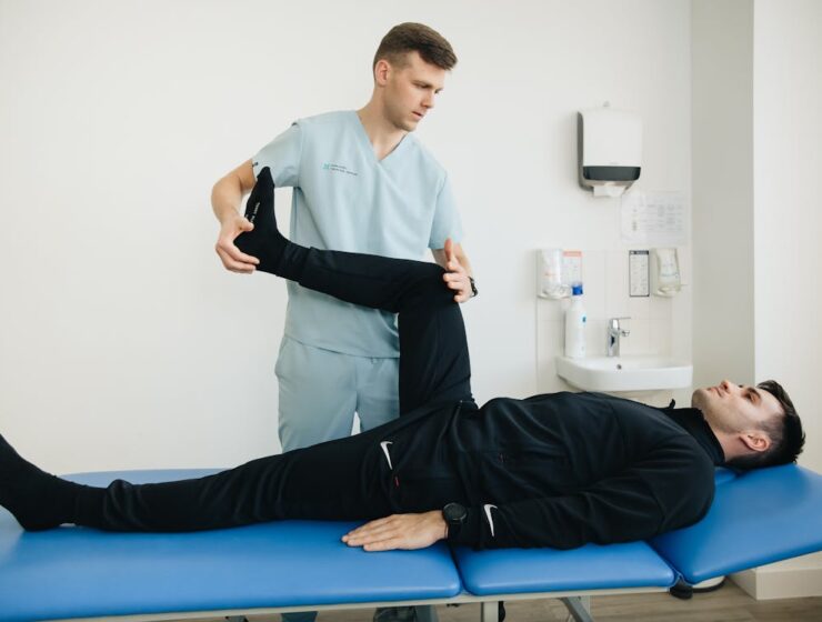Physiotherapist assisting a patient with leg stretching exercises on a treatment table in a clinic
