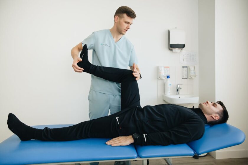 Physiotherapist assisting a patient with leg stretching exercises on a treatment table in a clinic